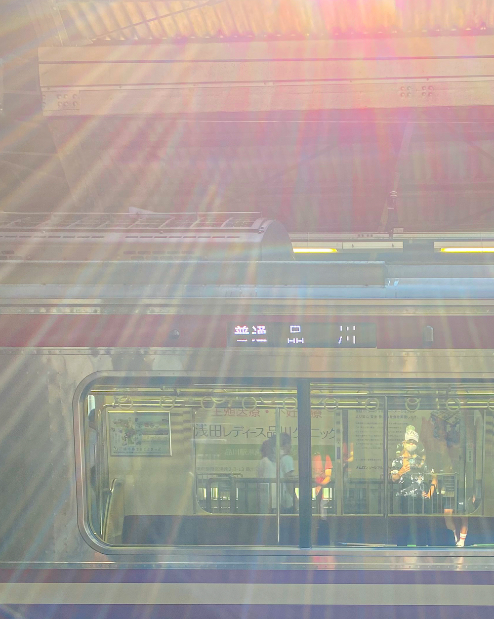 京浜急行・品川駅ホームで電車待ちしている際、向かい側のホームに停まった列車の窓ガラスに私が映っている。EMPORIO ARMANIの帽子を被っている。日光が光線となってホームに降り注いでいる。2022年7月22日。撮影：SHUN ROCKETDIVE